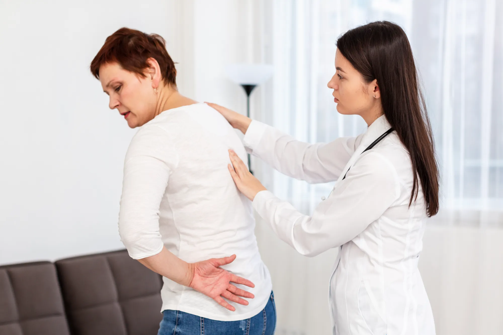 A female doctor feeling a woman's lower back in physical therapy