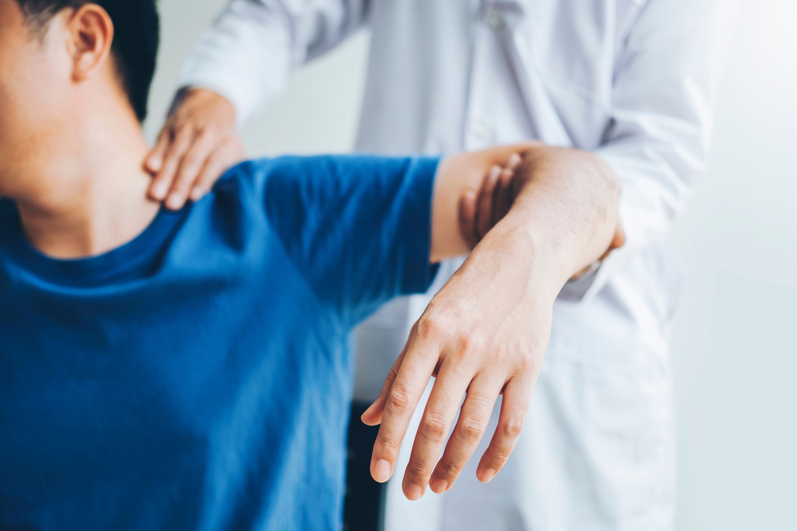 A close up of a doctor manipulating a man's arm and shoulder as part of an examination